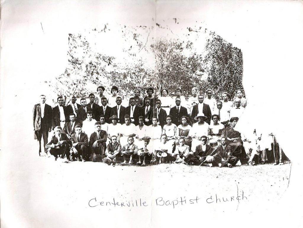 Black and white photo of a group of African American men, women, and children outside. Text written on the photo says Centerville Baptist Church.