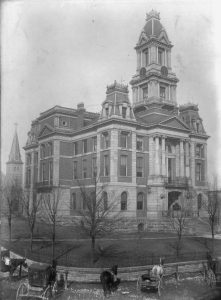 Black and white photography showing the 3rd Bourbon County courthouse. There are horses and wagons in the foreground.