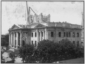 Black and white photograph showing ornate building under construction. A dome is in progress of being built. 